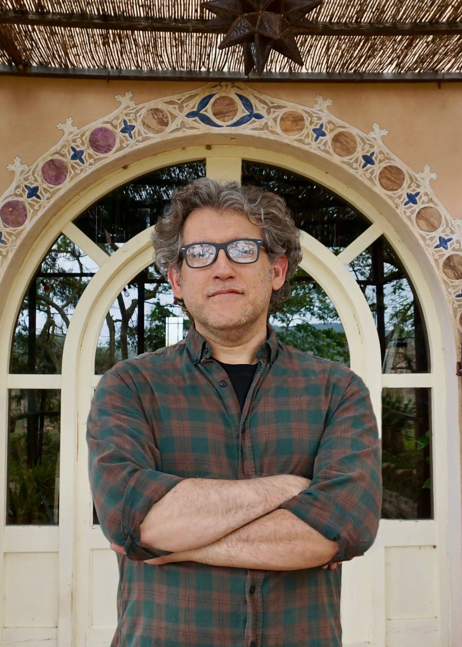 Man with glasses and plaid shirt standing in front of a decorative archway.