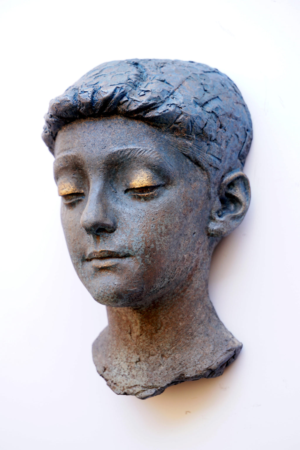 A textured sculpture of a young boy's head with closed eyes, mounted on a plain white wall.