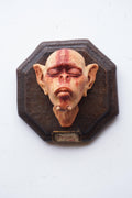 Decorative wall piece with a stylized face on an octagonal wooden frame.