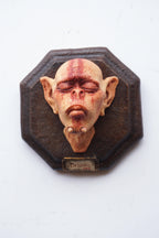 Decorative wall piece with a stylized face on an octagonal wooden frame.