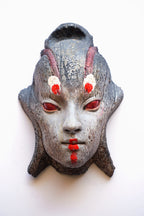 A textured, hand-carved Japanese-style mask with a weathered gray stone-like finish, featuring red eyes, red painted lips, and white and red markings on the forehead, shown against a plain white background.