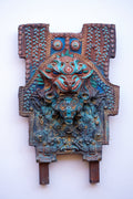 An ornate rectangular wall plaque featuring a sculpted face with turquoise, green, and bronze patina details, photographed against a plain white background.