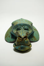 A sculptural monkey head mask or decorative object with a distressed turquoise, green, and brown patina finish, photographed on a plain white studio background.