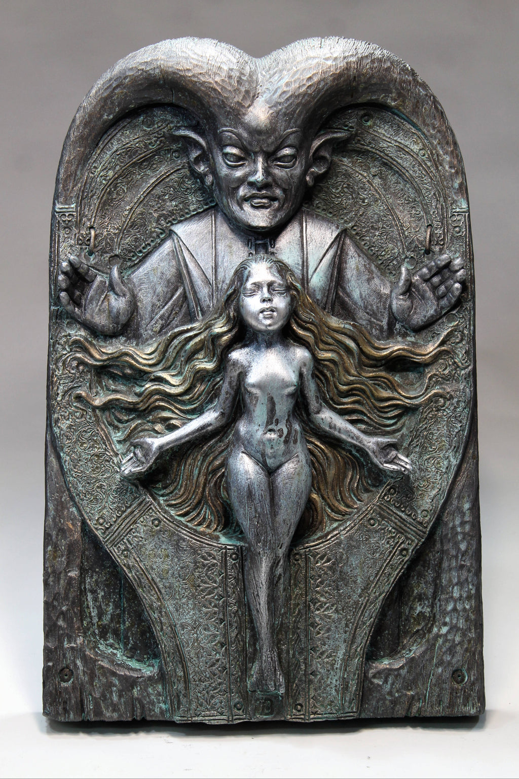 Bronze-like sculpture of a figure with ram's head and a woman below on a gray background