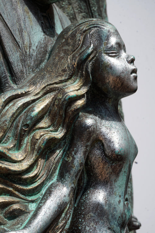 Bronze-like statue of a woman with flowing hair on a plain background