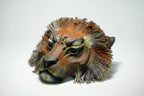 A sculptural lion head mask or decorative sculpture with textured fur details, shown on a plain light gray studio background.