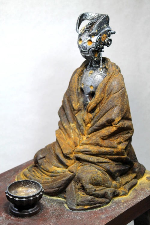 A sculpture of a seated monk automaton with a weathered robe and exposed mechanical details on the head and inner mechanisms.