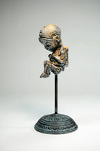 Metallic sculpture of a seated figure on a stand against a gray background