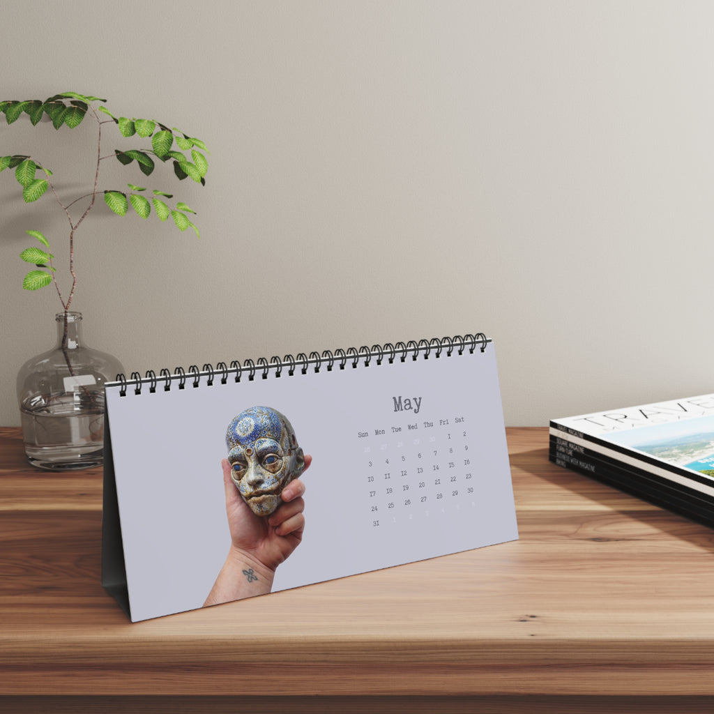 Calendar on a wooden surface with a decorative vase and plant in the background