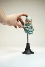 Hand holding a small sculpture of a baby on a white background